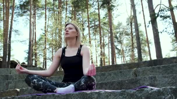 Szczęśliwa kobieta głęboko związana z naturą czuje jedność i medytację w lesie na świeżym powietrzu. Koncepcja. Blondynka w sportowym garniturze siedzi na betonowych schodach w medytacji w letni dzień. — Wideo stockowe