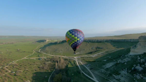 Vue de dessus du ballon coloré sur le champ vert. Fusillade. Boule colorée lumineuse se lève sur le champ vert à l'aube. Ballon se lève sur fond de champs verts et de montagnes à l'aube — Photo