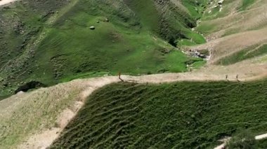 Yeşil dağ vadisinde yaz otlaklarında yürüyüş yapan turistler, hava manzarası. Başla. Yeşil yaz tepesinde yürüyen insanlar, seyahat ve macera kavramı.