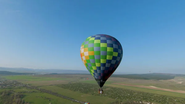 Blick von oben auf bunte Luftballons am Himmel. Schuss. Bunte Ballons fliegen über grüne Felder. Heißluftballonfahrt im Morgengrauen. Schöne Ballon fliegt auf dem Hintergrund von Feldern und blauem Himmel — Stockfoto