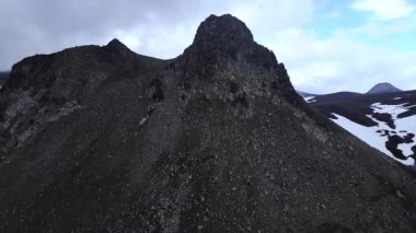 İnsansız hava aracı, karlı, çorak bir volkanik arazide engebeli, kayalık bir dağ zirvesine doğru uçuyor. Medya
