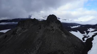 Drone camera approaching a rugged volcanic mountain peak surrounded by a desolate snowy landscape. Media