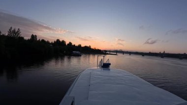 Sakin bir nehirde seyreden gemilerin manzarası gün batımında şehre doğru yelken açıyorlar. Kırp