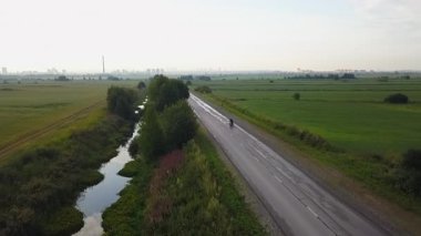 Bir yaz günü bir nehrin yanında kırsal bir yol boyunca giden bir motosikletlinin hava görüntüsü. Kırp