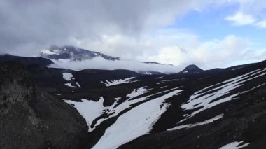 Issız bir arazide bulutlu bir gökyüzünün altında eriyen kar parçalarıyla dramatik volkanik vadi. Medya