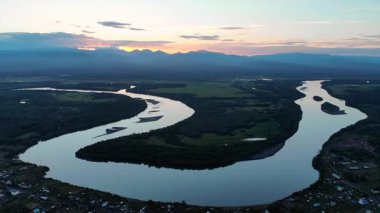 Gün batımında dağları olan bir vadiden akan geniş bir nehrin görkemli hava manzarası. Medya