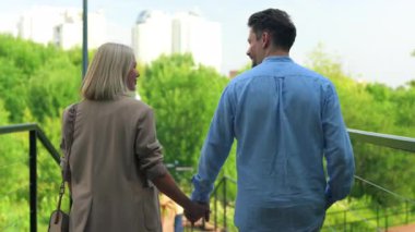 Bir şehir parkında merdivenlerden inerken el ele tutuşan ve konuşan bir çiftin arka görüntüsü.