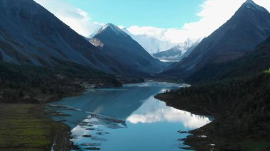 Serene turquoise lake nestled amidst towering peaks and lush forests, reflecting the sky. Media