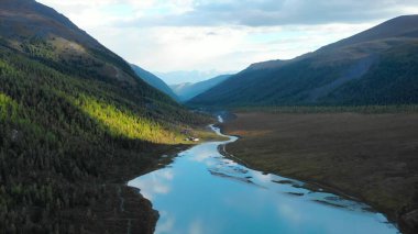 Majestic mountains surround a turquoise river flowing through a valley with autumn colors. Media