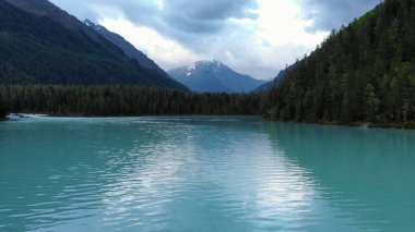 Turkuaz su dağları ve bulutlu gökyüzünü yansıtır. Medya