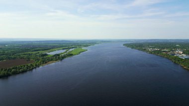 Nehir açık mavi bir gökyüzünün altında yeşil bir arazide akar. Kırp