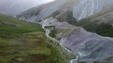 Turquoise river meandering through a valley surrounded by mountains and colorful vegetation. Media