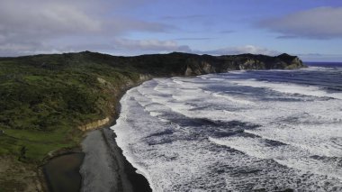 Siyah kum, dramatik uçurumlar ve güçlü okyanus dalgalarıyla nefes kesici Whatipu sahili manzarası.