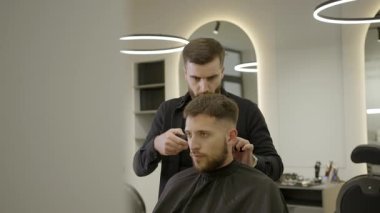 Modern bir berber dükkanında genç bir adamın saçını yapmak için elektrikli makas kullanıyor. Kırp