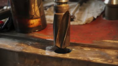 Metal bir yüzey üzerinde dönen matkap ucu, atölye ortamında çalışmaya hazır