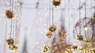 Parlak noel ışıkları ve dekorasyonları bir şehir sokağının üzerinde asılı, neşeli bir atmosfer yaratıyor.