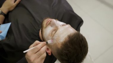 Güzellik uzmanı, güzellik salonundaki bir adamın yüzüne nemlendirici yüz maskesi uyguluyor. Kırp