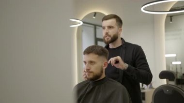 Erkek kuaför modern bir berber dükkanında saç kesimi sırasında bir adamın saçını tarıyor ve şekillendiriyor. Kırp
