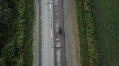 Yeşil tarlalarla çevrili kırsal bir asfalt yolda kruvazör bisikleti süren yalnız bir motosikletçi. Kırp