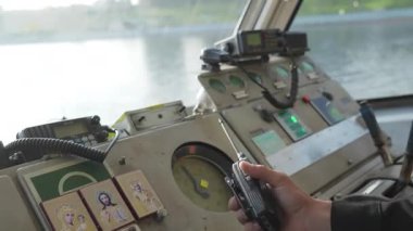 Üniformalı genç bir denizci bir teknede geziniyor ve kokpitteki el telsizine konuşuyor. Kırp