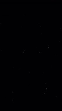 Küçük beyaz parçacıklar yavaşça siyah bir arkaplanda yüzerler.