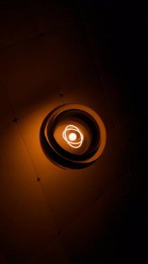 Parlayan turuncu atom sembolü koyu renkli bir zemin üzerinde cam bir küre içinde dönüyor.