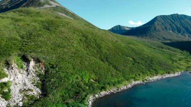 Hava uçuşu, güneşli bir günde açık mavi okyanus suyuyla buluşan güzel bir yeşil dağ sırasını gösteriyor. Medya
