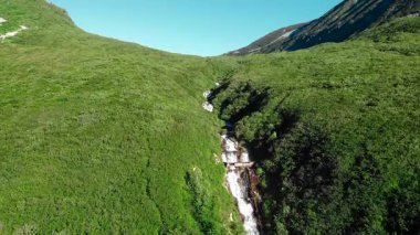 Şelale gibi çağlayan bir şelaleyle çarpıcı bir dağ vadisinde geriye doğru hareket eden hava görüntüleri. Medya
