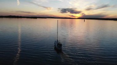 Güzel ve renkli bir günbatımında sakin bir gölde seyreden yalnız bir yelkenli.