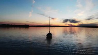 Sakin sularda yüzen siluetli yelkenli. Yüzeye yansıyan güzel bir günbatımı.