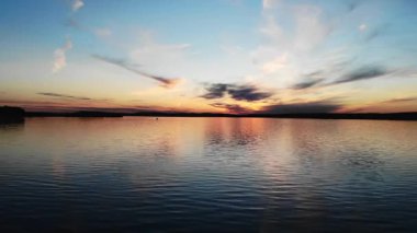 Sakin su yüzeyi, güzel ve huzurlu bir gün batımında gölün üzerinde renkli bir gökyüzünü yansıtıyor.