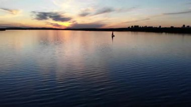 Sakin bir gölde yüzen yalnız yelkenli. Durgun suya yansıyan renkli bir günbatımı var.