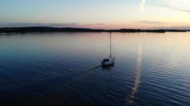 Renkli bir günbatımında sakin bir göl boyunca seyreden yalnız bir yelkenlinin havadan görüntüsü.