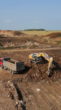 Büyük bir kazıcı inşaat alanındaki bir çöp kamyonuna toprak yüklüyor.