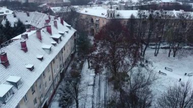 Sakin bir şehir avlusundaki apartmanlar arasında karlı bir yolda giden bir arabanın hava görüntüsü. Medya