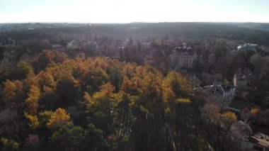 Güneşli bir günde, sonbahar yaprakları ve büyüleyici evlerin olduğu manzaralı bir ormanın üzerinden uçmak. Medya
