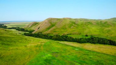 Parlak bir yaz gününde yemyeşil tepeler ve çayırlar üzerinde uçan manzara görüntüleri. Medya