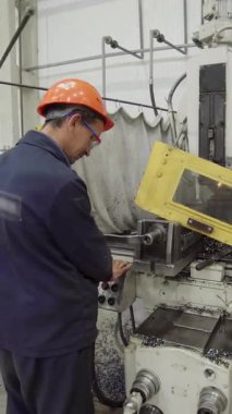 Güvenlik gözlüğü takan fabrika işçisi değirmen makinesini çalıştırıyor, metal talaşı üretiyor.