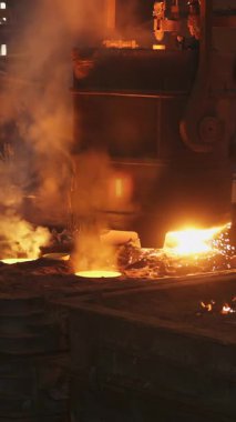 Dökümhaneye erimiş metal döken çelik işçileri kıvılcım ve duman yaratıyor.