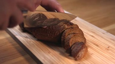 Erkek eller, bir somun koyu çavdar ekmeğini tahta kesme tahtasındaki bıçakla dilimlere ayırıyor. Medya