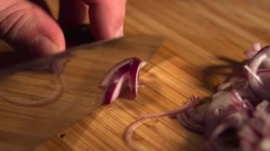 Bambu kesme tahtasındaki taze kırmızı soğanı dilimlemek için bıçak kullanan bir aşçının ellerini kapatın. Medya