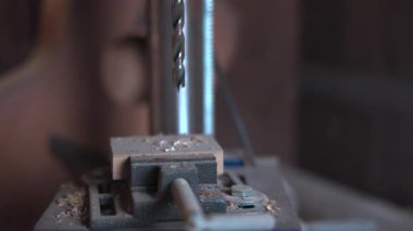 Endüstriyel matkap ucu ucu, mengeneye sıkıştırılmış ahşap bir bloğa doğru dönüyor ve iniyor. Medya