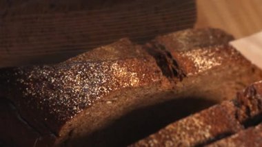 Ahşap bir kesme tahtasıyla taze, koyu bir çavdar ekmeğini dilimleyen bir insan eli. Medya