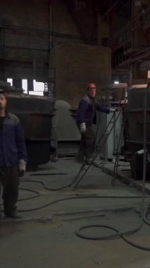 Endüstriyel işçiler bir metal dökümhanesinde, erimiş metal dökme ve dökme sürecini gösteren bir fırın işletiyorlar.