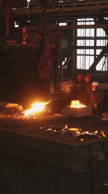 Dökümhane işçileri büyük bir endüstriyel kalıba erimiş metal döküyorlar.