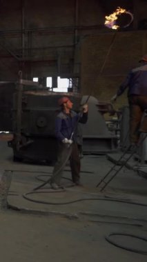 Dökümhane işçileri metal döküm yapıyor, endüstriyel ortamda erimiş metalleri kalıplara döküyorlar.