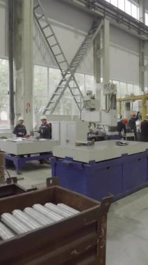 Fabrika işçileri modern bir endüstriyel tesiste büyük bir makinede metal parçaları birleştiriyorlar.