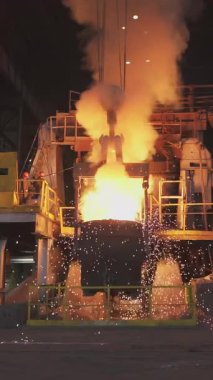 Çelik fabrikasındaki büyük bir konteynırdan dökülen erimiş metal kıvılcımlar ve duman yaratır.