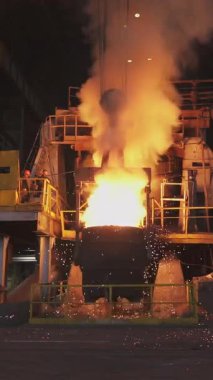 Çelik fabrikasındaki büyük bir konteynırdan dökülen erimiş metal kıvılcımlar ve duman yaratır.
