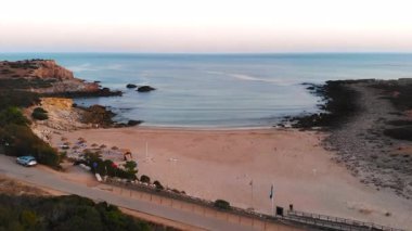 Güneşin doğuşuyla birlikte kumlu sahil koyuna ve nazik dalgalara, dağınık şemsiyelere ve park edilmiş arabalara. Medya